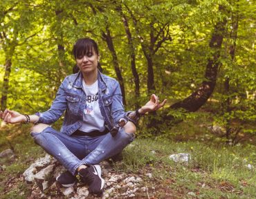 A woman meditates peacefully in a lush green forest, exuding calm and relaxation.